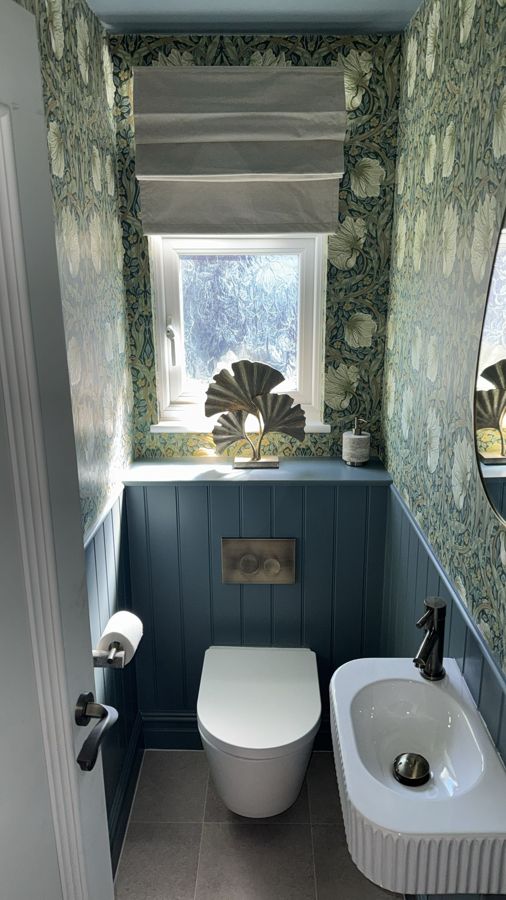 Cloakroom with blue tongue-and-groove panelling, wall-hung toilet, fluted basin and floral wallpaper